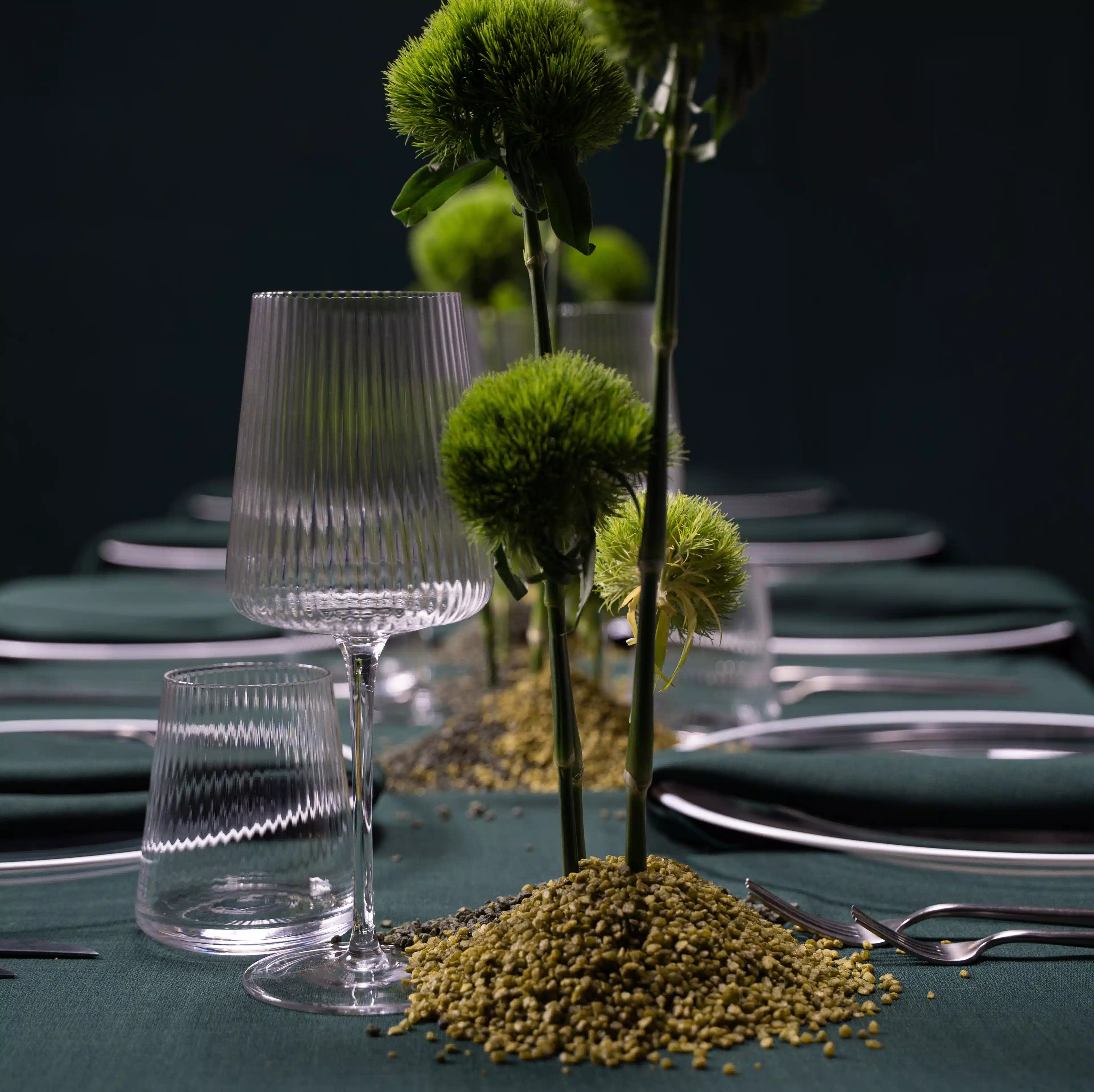 Clear Lined Glassware Collection on a green tablecloth, featuring ribbed wine and water glasses, complementing a minimalist centerpiece with sculptural, chartreuse-green flowers.