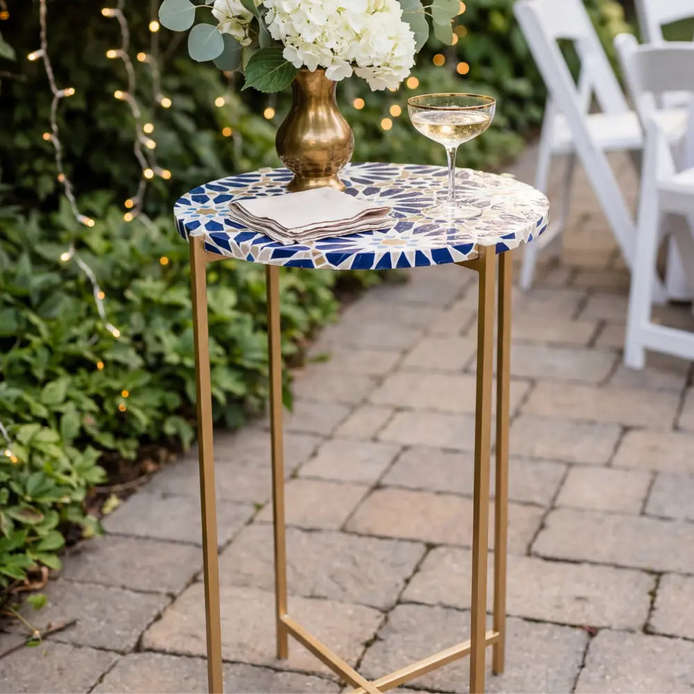 Metal Legs w/ Tabletop Cocktail Table with gold base and blue mosaic top, adorned with napkins, drink, and vase, on a patio setting.
