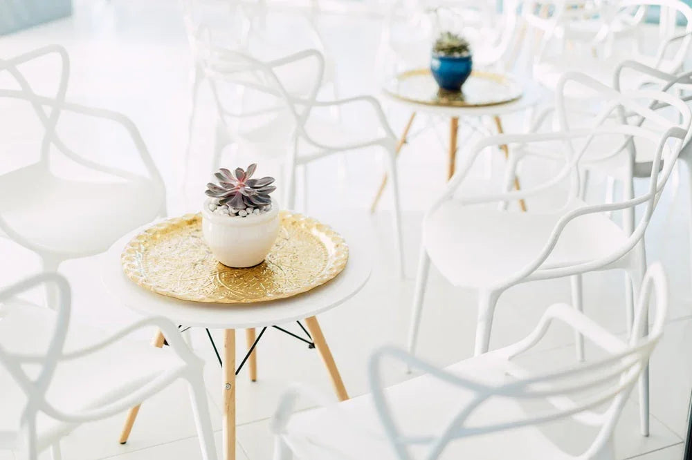 Masters Chair White Replica, elegant white chairs ideal for events. Displayed with a potted plant on a gold tray, showcasing a sleek, modern design.