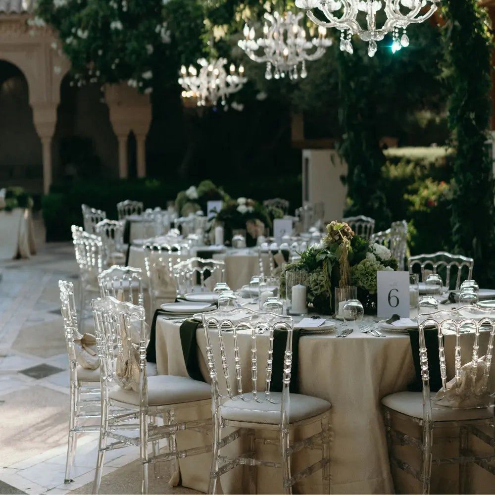 Elegant outdoor setup featuring NAPOLEON ACRYLIC CHAIR, blending timeless design with modern transparency, surrounding tables set for a formal event with glassware and floral centerpieces.
