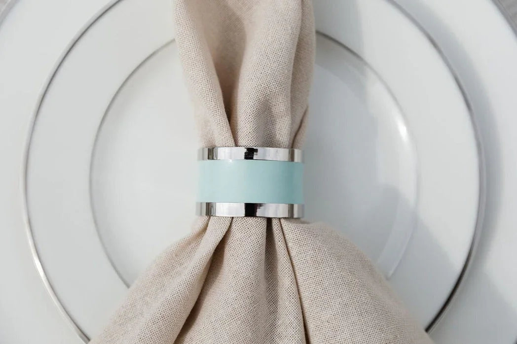 NAPKIN RING - SILVER & AQUA ROUND on a plate, showcasing a simple, elegant design suitable for enhancing any tablescape.