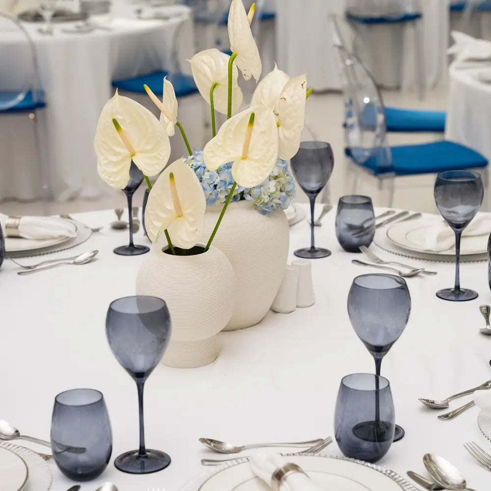 Off White Lined Pot holds white anthuriums and blue hydrangeas on a formally set dining table, enhancing elegant event decor.