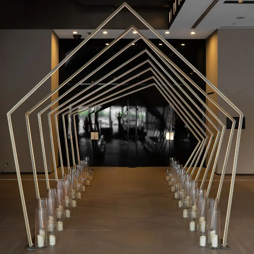 PENTAGON TUNNEL WITH COLOR CHANGING LED: Modern gold pentagon arches forming a tunnel, featuring color-changing neon lights, ideal for event entrances.