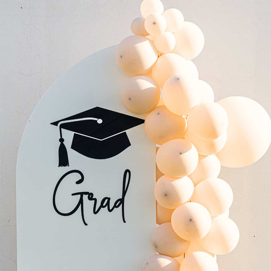 Sweet Soirée Balloon Arrangement featuring a cream arch backdrop with Grad print and cascading peach balloons, perfect for adding elegance to graduation celebrations.
