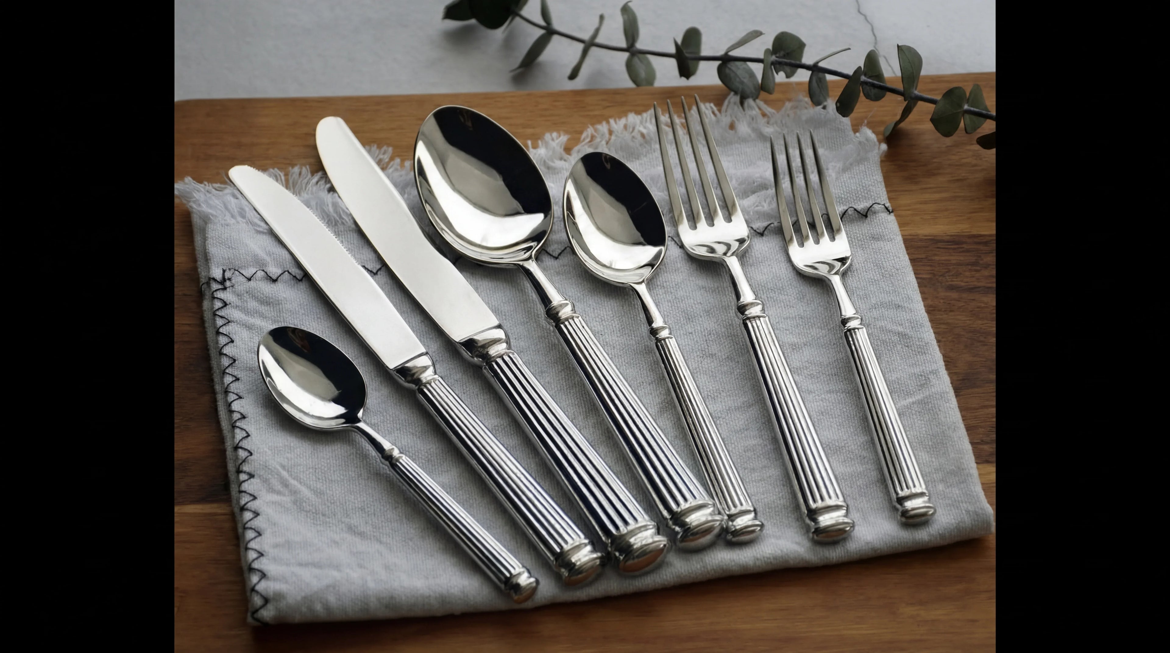 CUTLERY MODERN SILVER: Polished, fluted-handle flatware set on a cloth napkin, ideal for elegant events and refined celebrations.