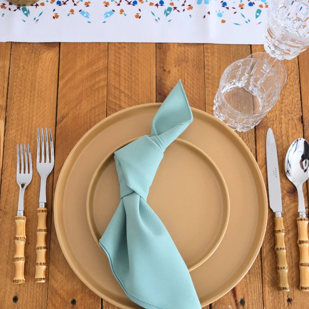 Mustard Ceramic Matte Plates set on a wooden table with bamboo-handle cutlery, teal napkin, and cut-glass tumblers, showcasing modern simplicity for elegant dining.