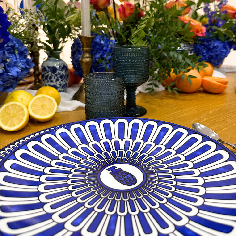Geometric Blue Plates featuring a pineapple motif in a styled tabletop setting with hobnail goblets, a brass candlestick, and a floral arrangement.