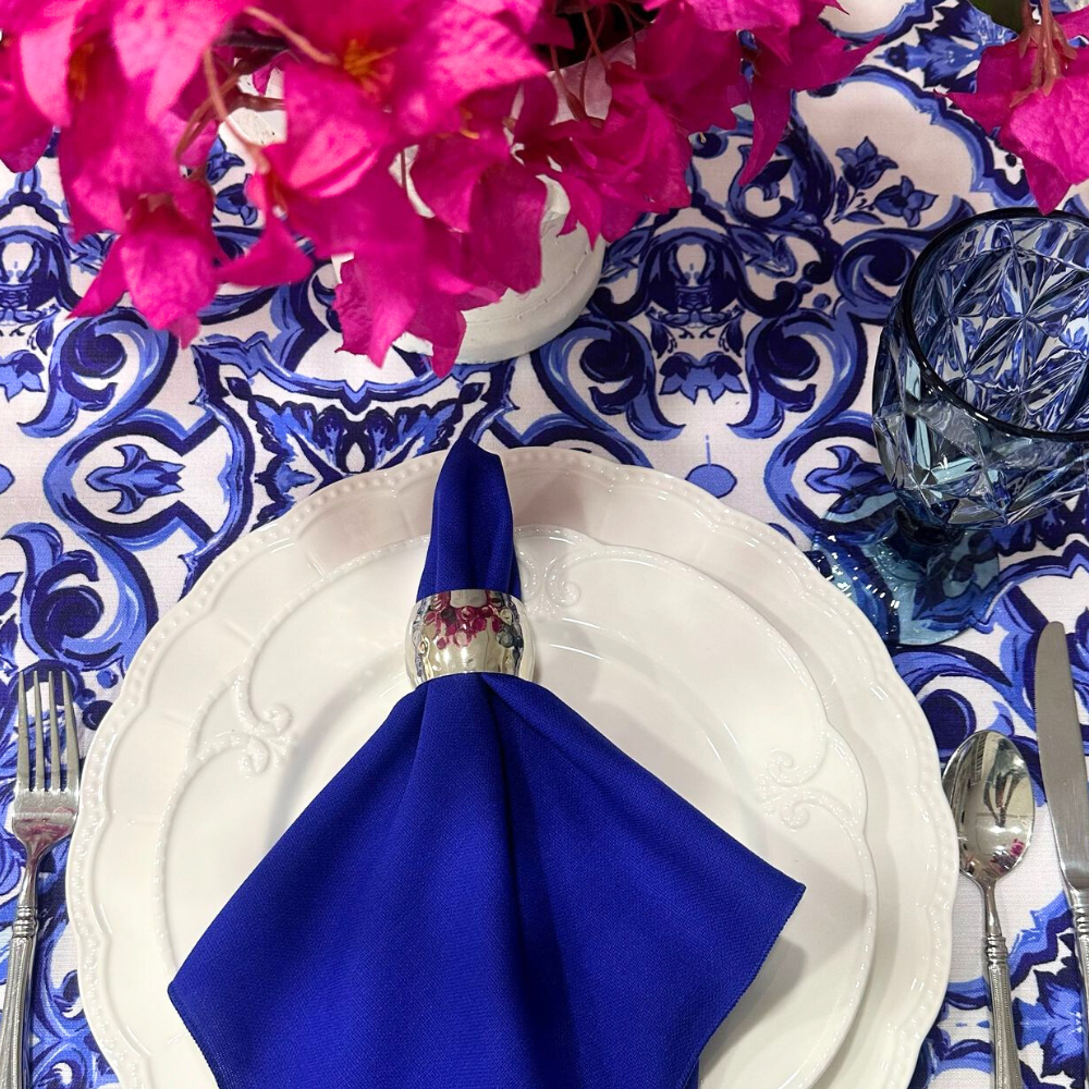Silver hammered dome napkin ring on a white plate with a blue napkin, complemented by a vase of pink flowers, ideal for elegant table settings.