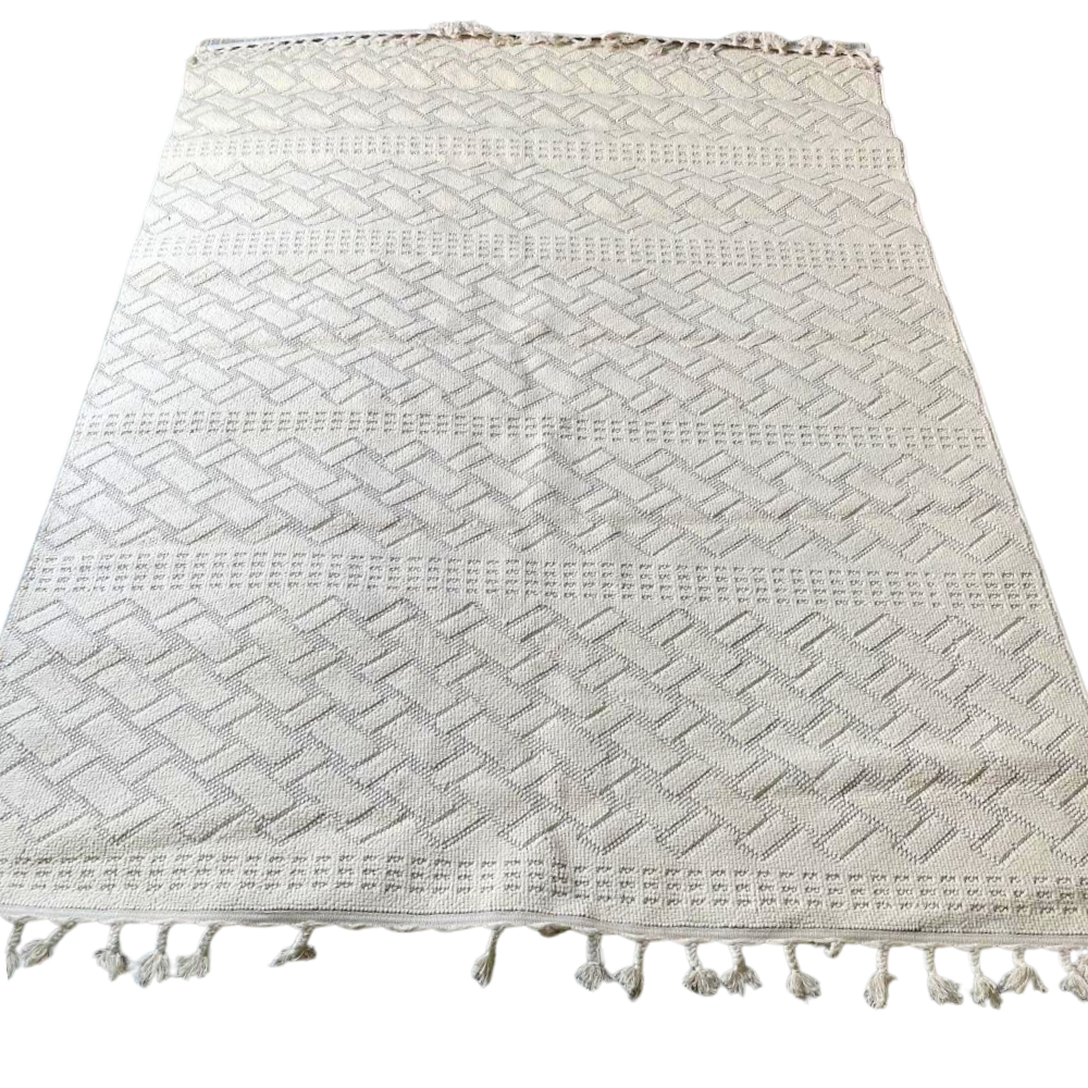RUG NATURAL WOVEN: A light-cream rectangular textile with a herringbone pattern and knotted tassels, crafted from eco-friendly jute for a timeless, organic look.