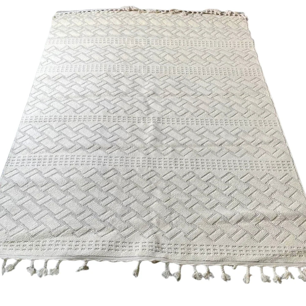 RUG NATURAL WOVEN: A light-cream rectangular textile with a herringbone pattern and knotted tassels, crafted from eco-friendly jute for a timeless, organic look.