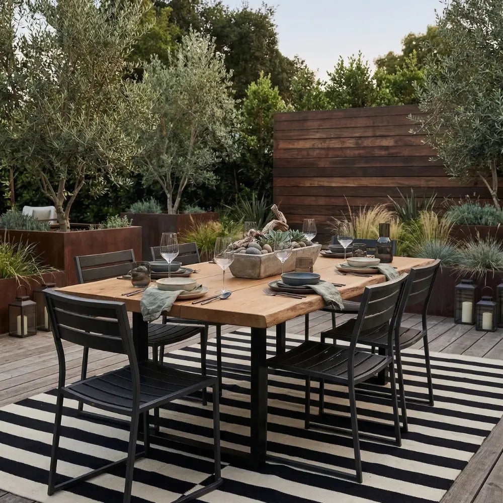 RUG BLACK AND WHITE STRIPES anchors an outdoor dining setup, enhancing the space with its bold pattern under a wooden table surrounded by metal chairs.