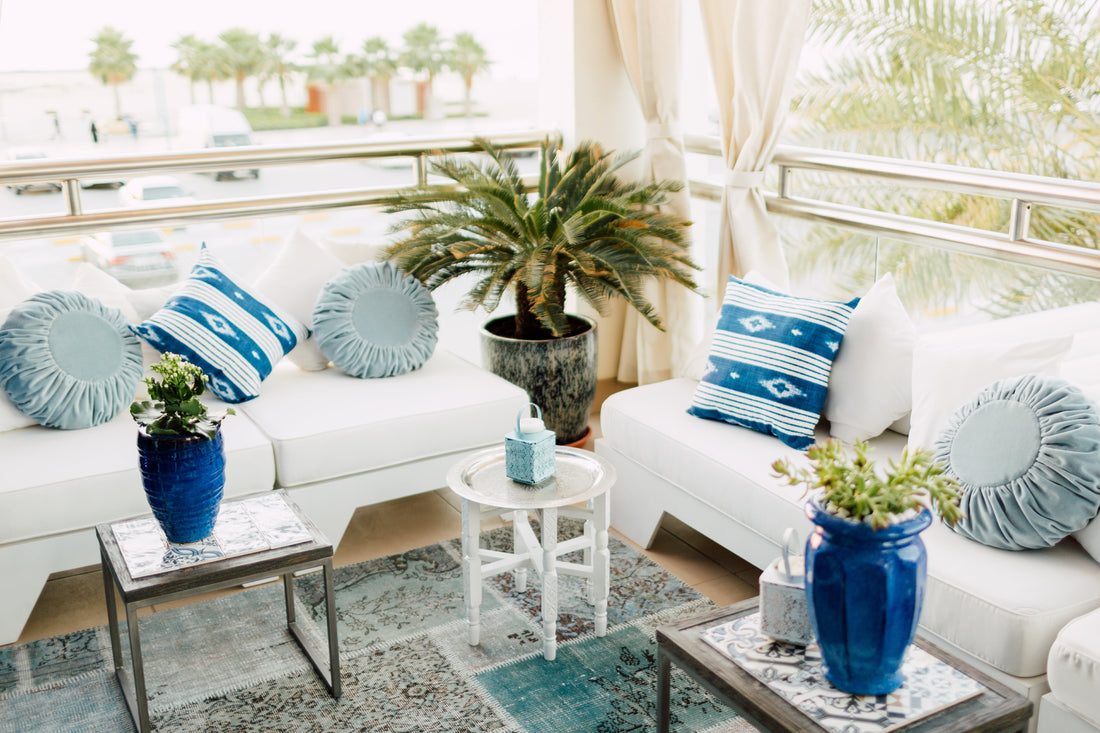 Round pleated textured velvet cushion on a white couch, enhancing a luxurious patio setup with complementary blue and white pillows and decor elements.