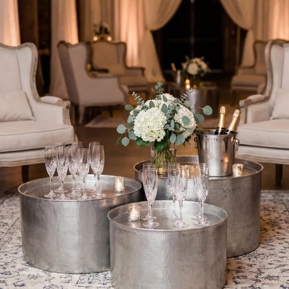 ALUMINIUM COFFEE TABLES in a party setup, featuring three hammered metal tables with champagne flutes and candles, enhancing an elegant lounge environment.