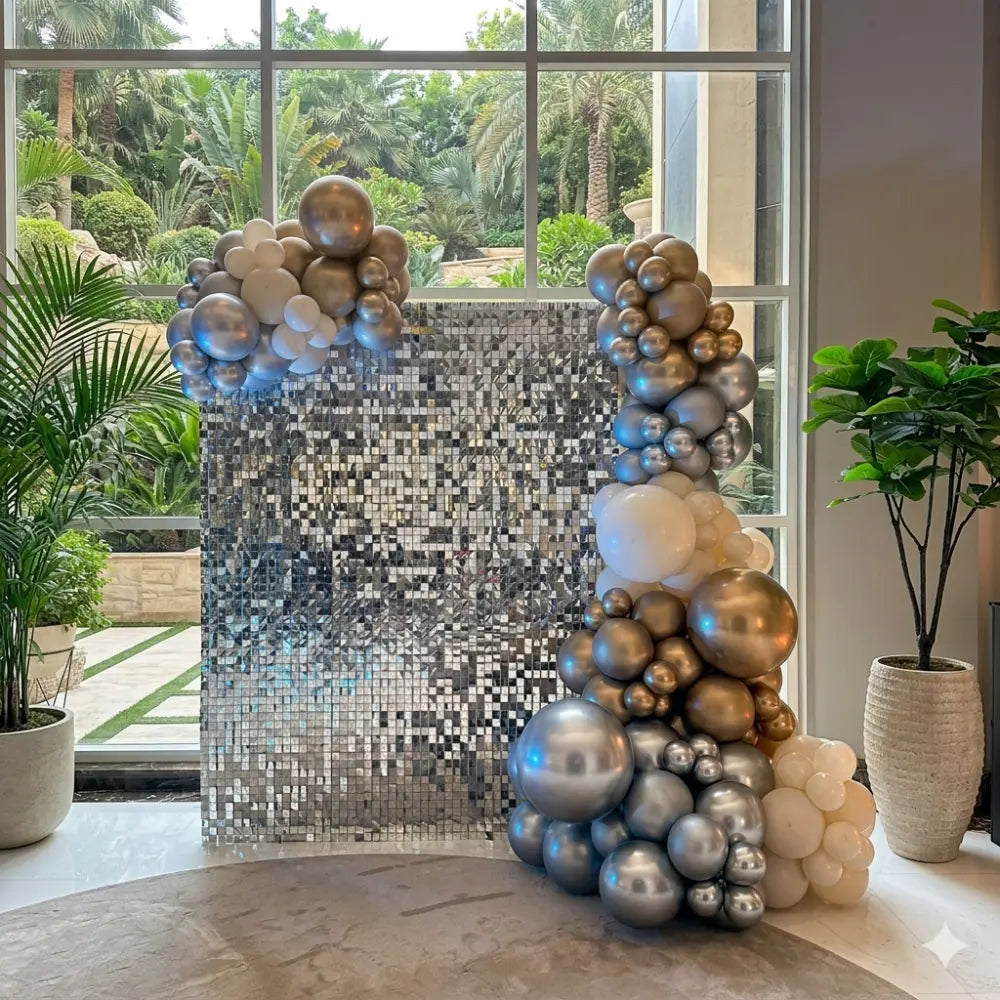 Sequin Wall backdrop with mirror-like tiles, perfect for events. Adorned with balloon garland and flanked by potted plants, offering elegant decor versatility.
