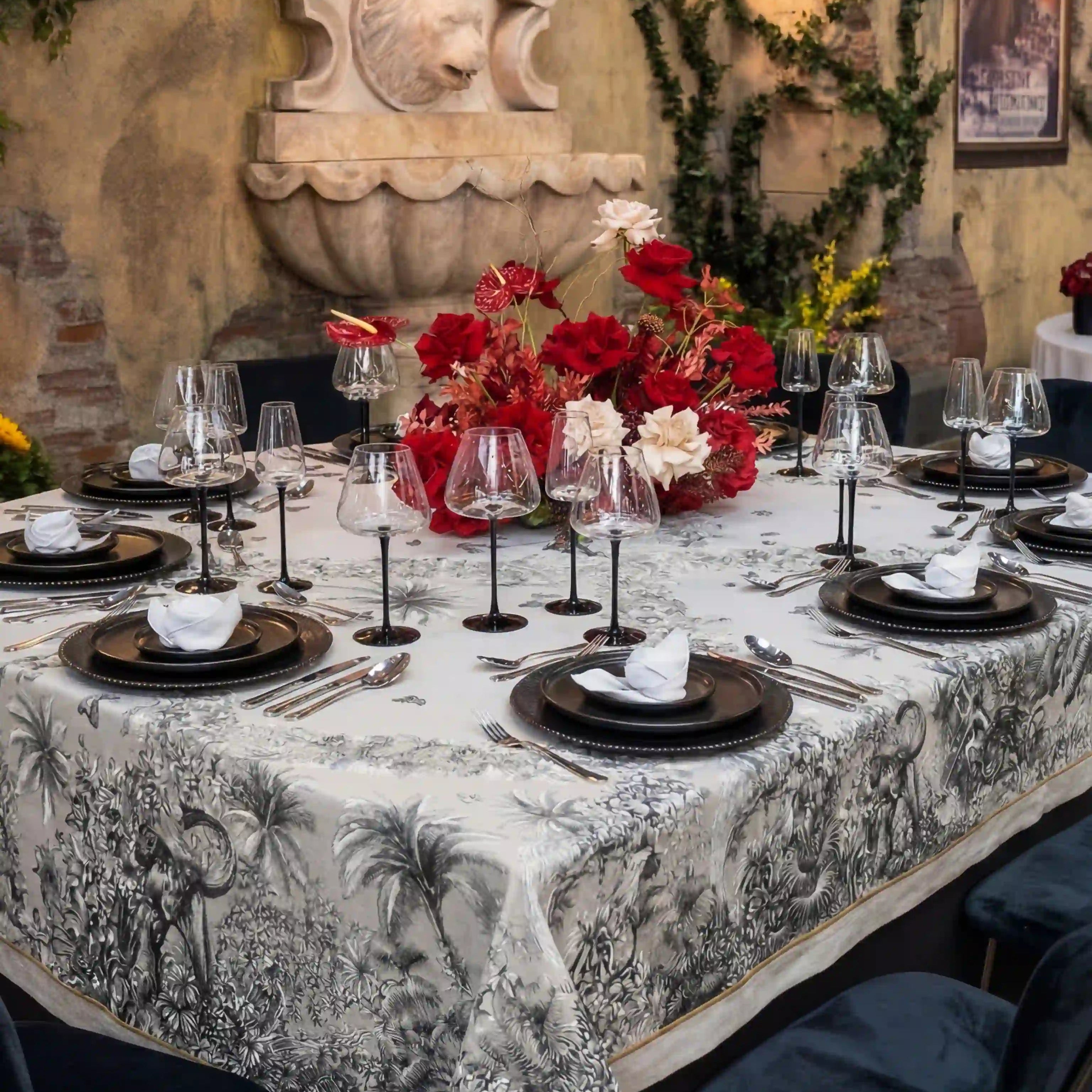 Elegant dining setup featuring the Savannah Toile Linen Tablecloth with intricate pastoral scenes, surrounded by lush floral centerpiece and sophisticated table settings.
