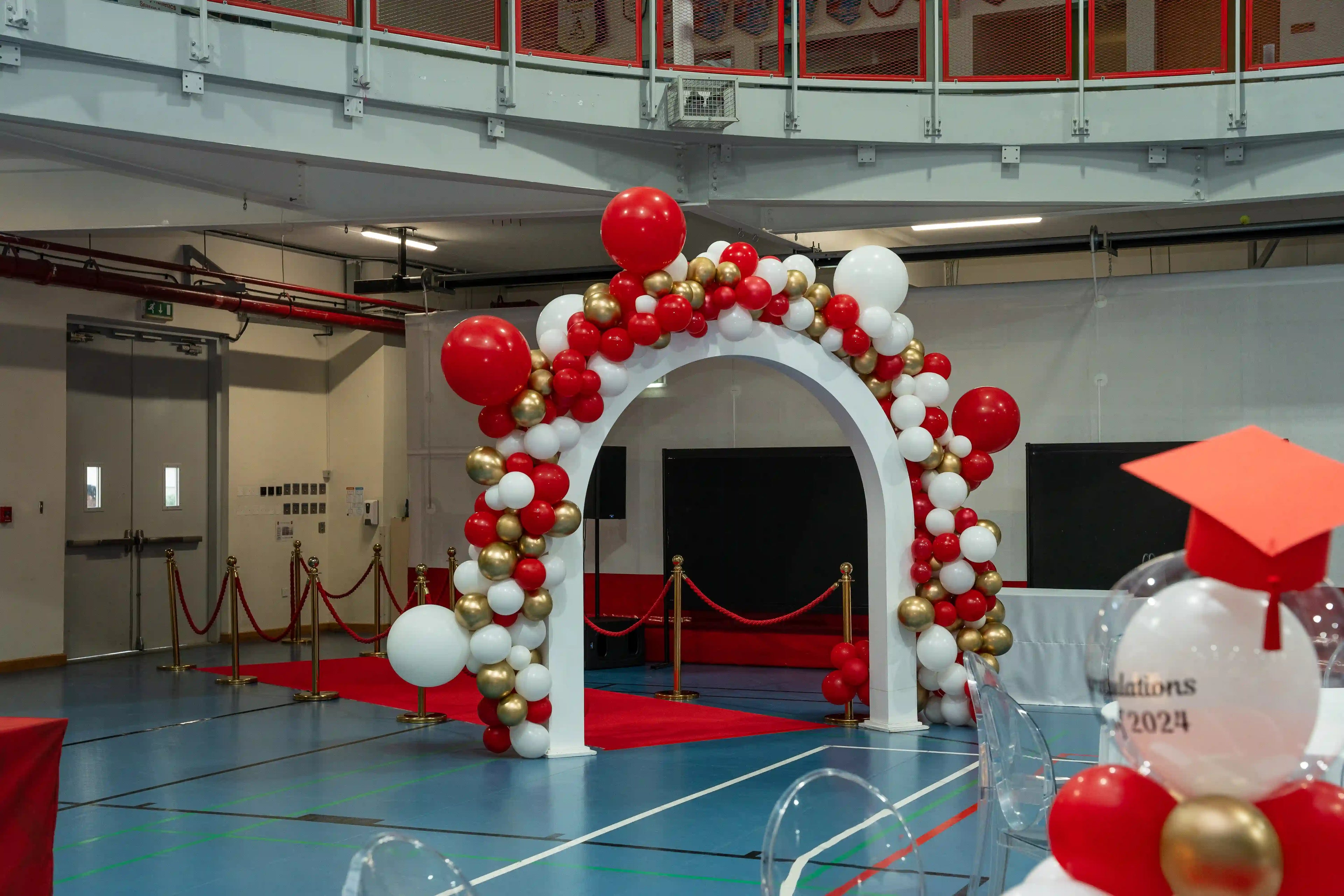 Grand Celebration Balloon Arch featuring a white arch with red, white, and gold balloons, creating an elegant entrance for events like graduations and ceremonies.