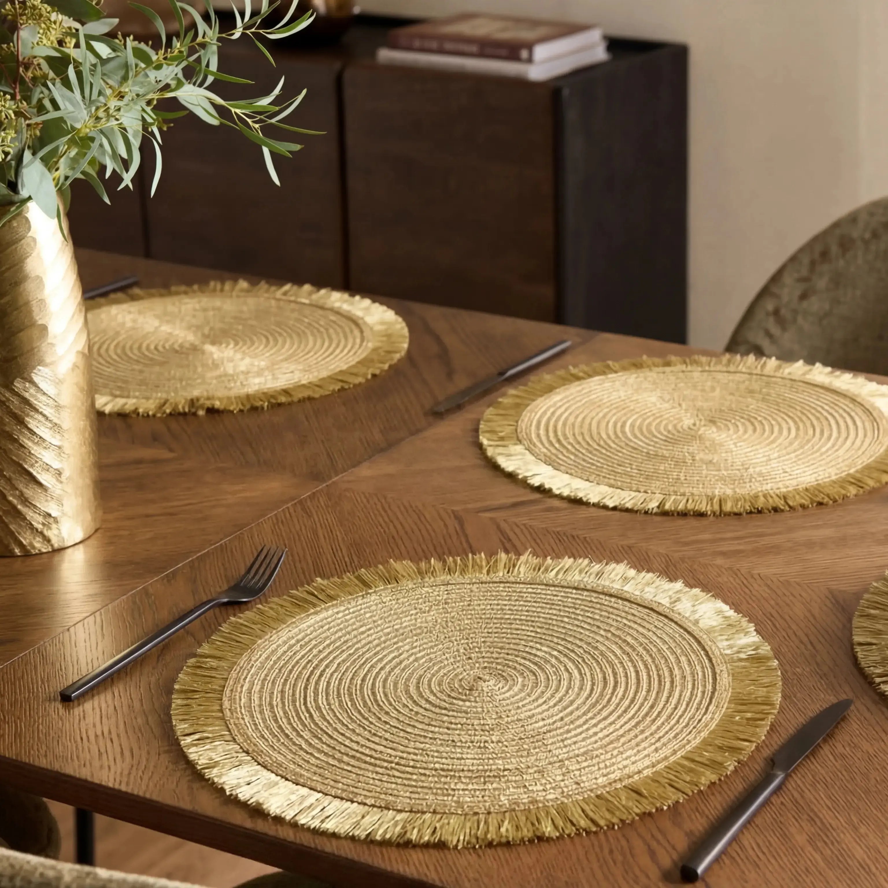 Gold woven placemats on a wooden table with cutlery
