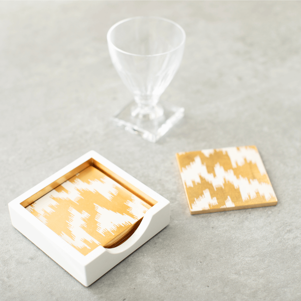 A modern Moiré square lacquer coaster set of 4 in a sleek holder, featuring glass and a white-gold box on a table. Handmade in Vietnam, showcasing art from renowned collections.
