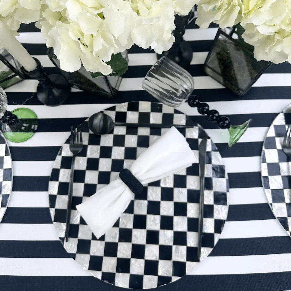 Round Shell Patterned Placemat in Black & White Color, 1 each, displayed on a table with black and white plates, a folded napkin, and a vase with white flowers.