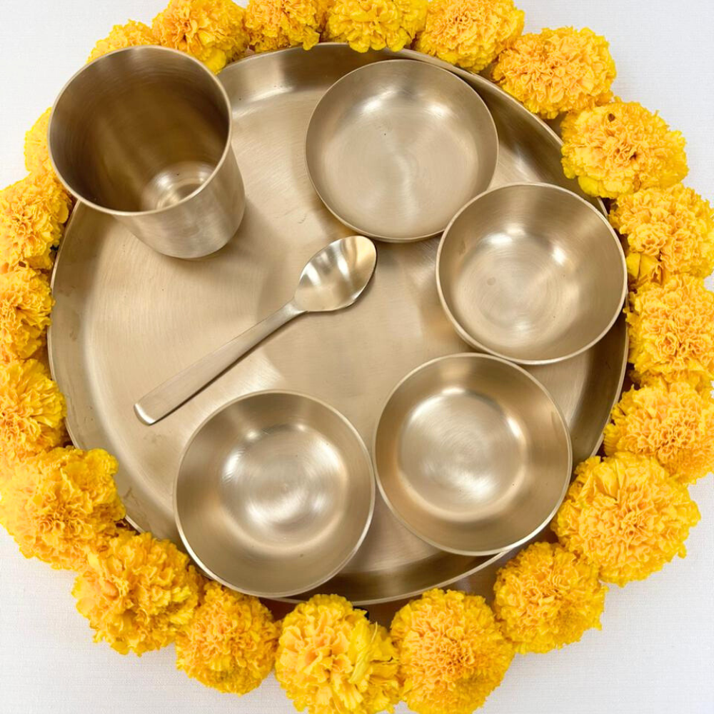 Diwali Thali Gift Box featuring cups, bowls, and spoons arranged on a tray surrounded by yellow flowers, perfect for festive gifting.