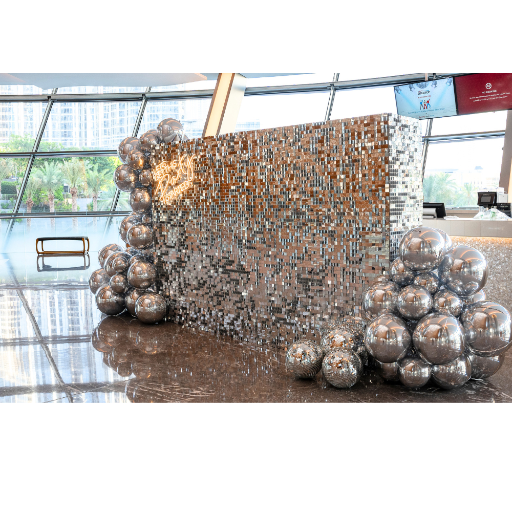 Silver Sequin Wall Balloon Backdrop with LED Neon Sign, featuring shiny silver balls, ideal for events like weddings and parties.