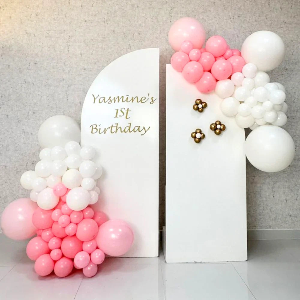Semi Arches Balloon Backdrop on display against a wall, featuring a white sign with gold text and decorative white and gold flower magnets.