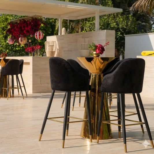 VELVET STOOL BLACK: A high-top table with black velvet bar stools featuring gold accents, creating a sophisticated, modern look ideal for elegant cocktail setups.