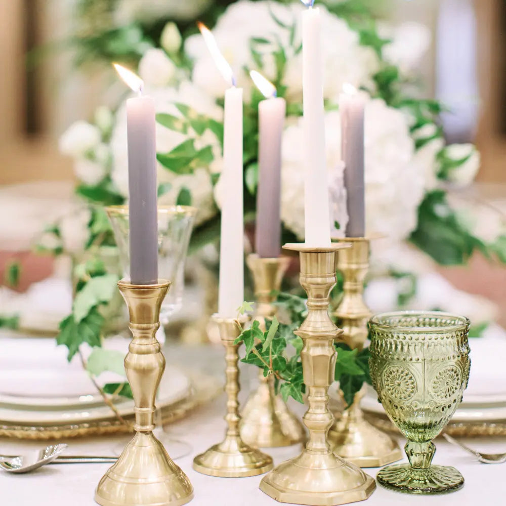 Decorative table setting with gold candlesticks, white candles, and green glassware.