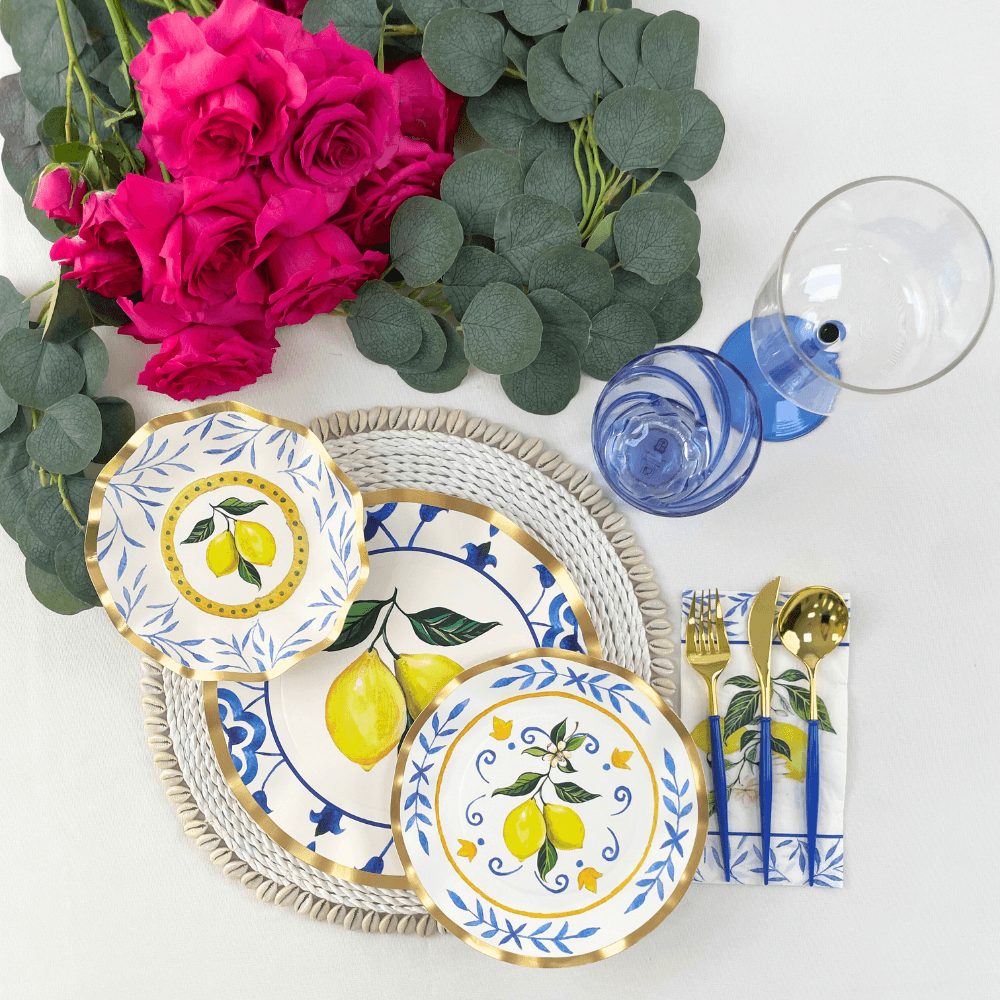 Capri Coast Paper Salad & Dessert Plate- 8 Per Package: Elegant plates with blue pattern, lemons on white background. Perfect for events. Image: Table with plates, flowers, blue liquid, gold utensils. Store: Party Social - Your go-to for party essentials.