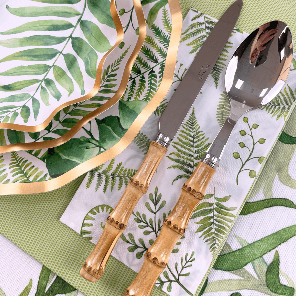 Fern & Foliage Paper Guest Towel Napkins on a napkin with a spoon and knife. Elevate your party with elegance. Perfect for any event. From Party Social, your go-to for party essentials.