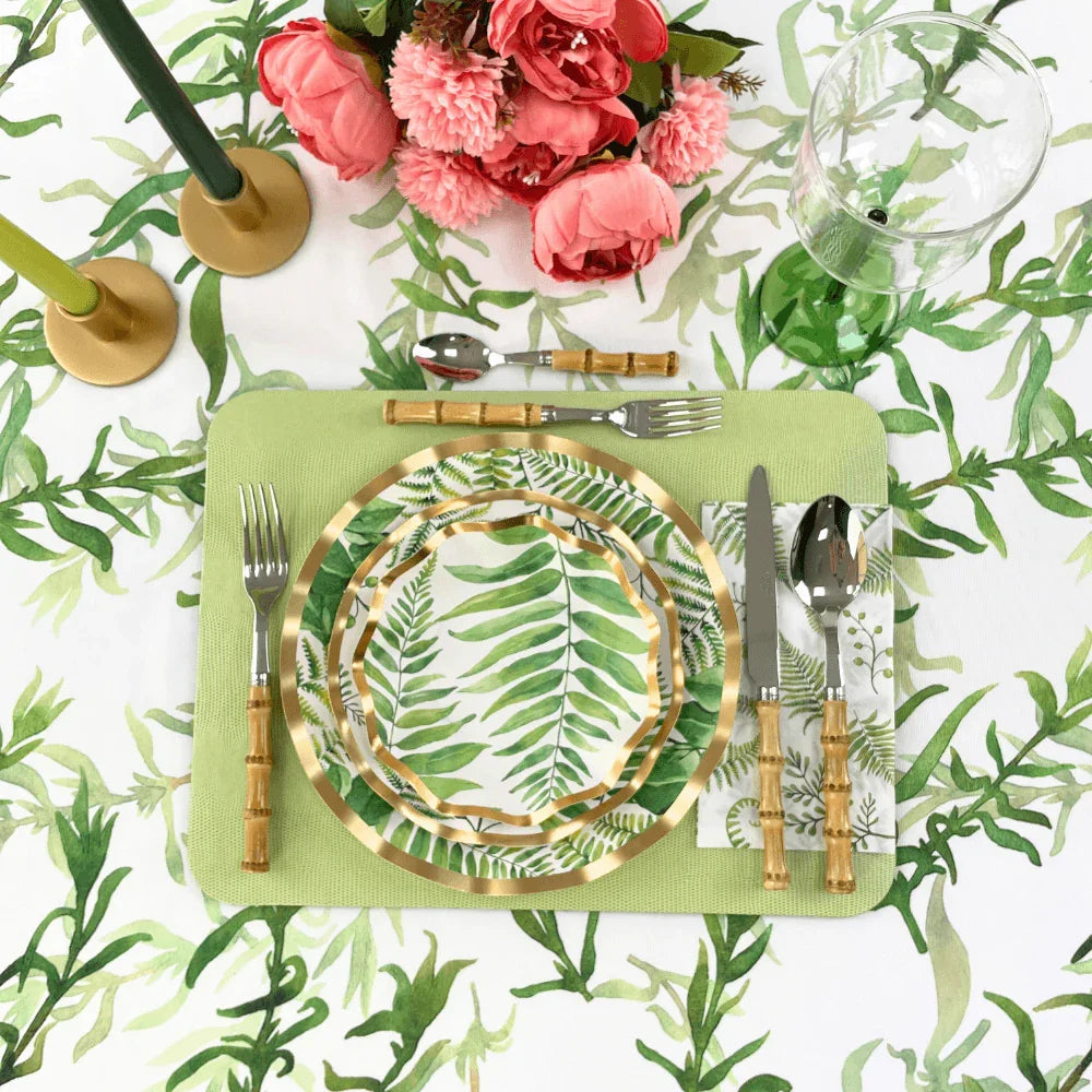 Fern & Foliage Paper Guest Towel Napkins-20 Per Package displayed with a plate, silverware, and a glass on a table, complemented by pink flowers and a stack of plates with leaf designs. Ideal for adding elegance to any party setup.