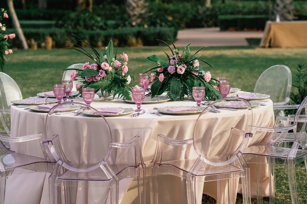 GHOST CHAIR WITH ARMS (LOUIS) elegantly set at a dining table, showcasing its versatile design amidst a dinner party arrangement with floral centerpiece.