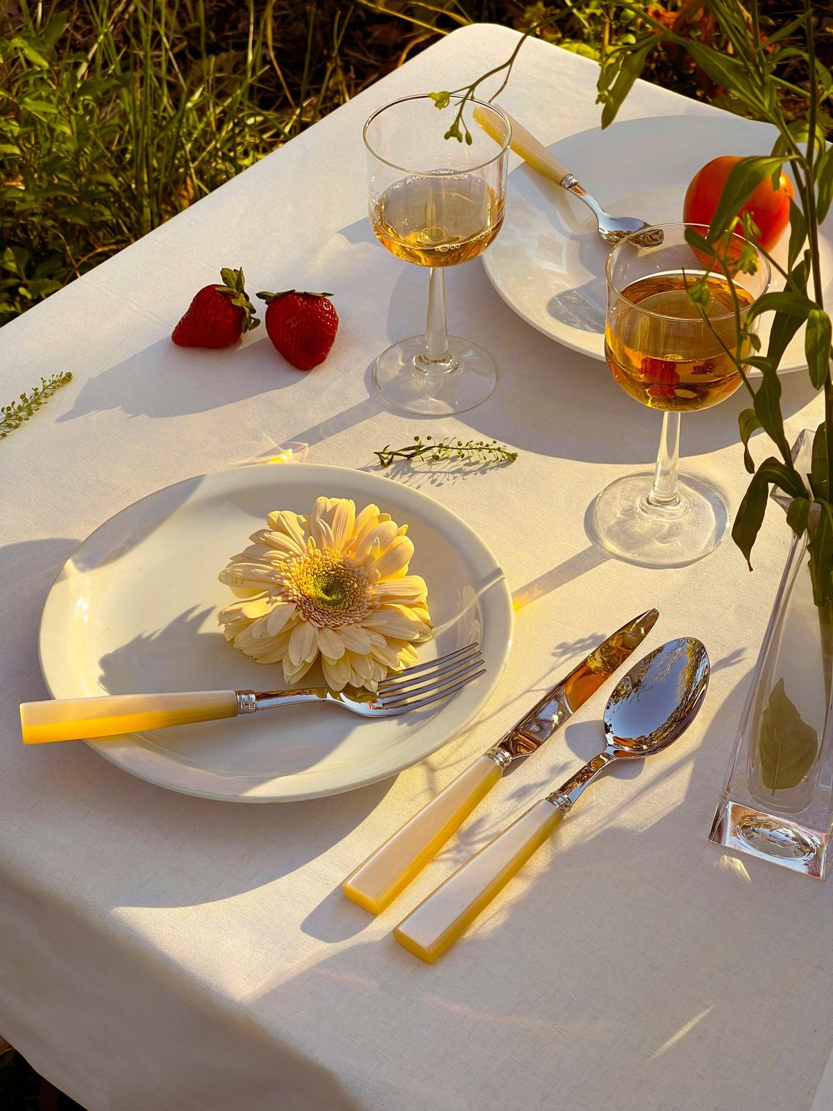 Pearl Cutlery Set of 5 on a table with a yellow flower on a plate, accompanied by wine glasses.