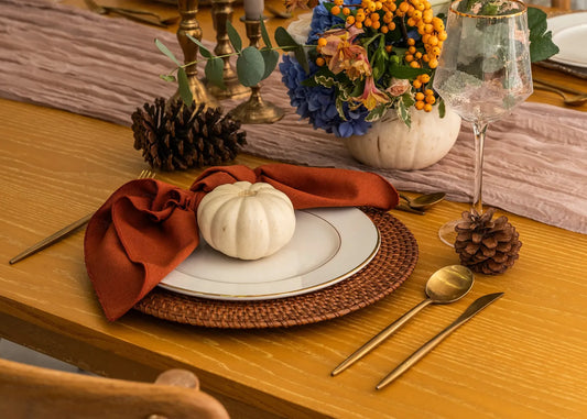 CHARGER PLATE - RATTAN on a fall-themed table setting with gold-rimmed dinnerware, a mini-pumpkin, brass flatware, and a rustic centerpiece.