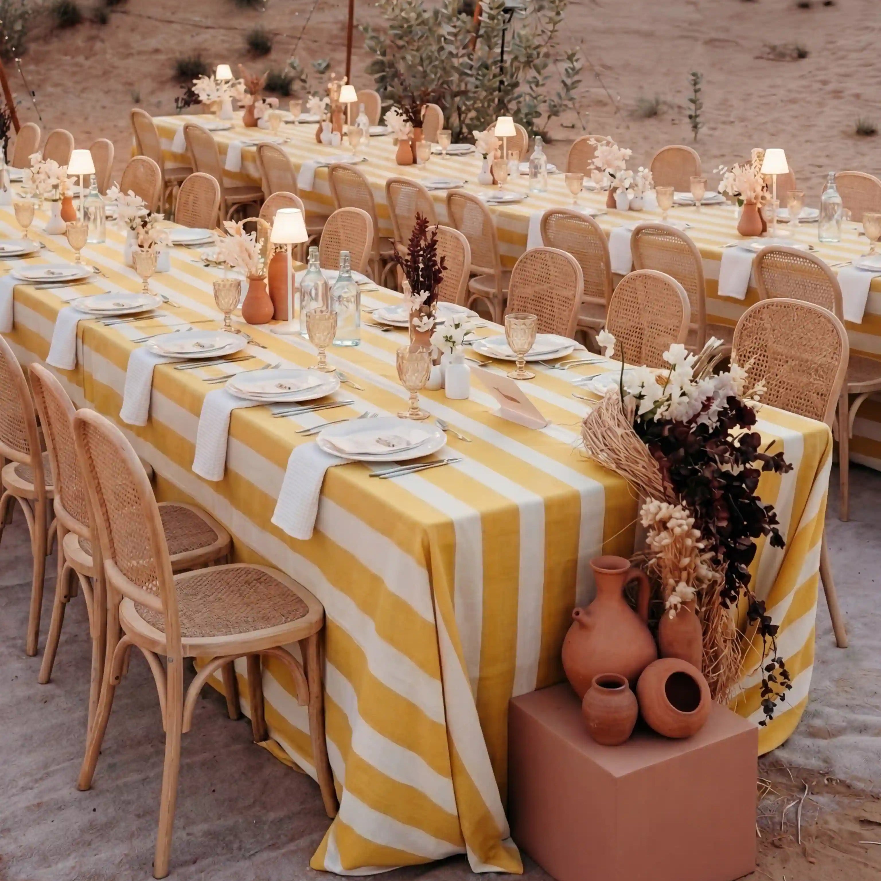 Yellow Stripe Linen Tablecloth graces a boho-chic desert banquet, draped over two long tables with rattan chairs, enhancing the outdoor dining ambiance.