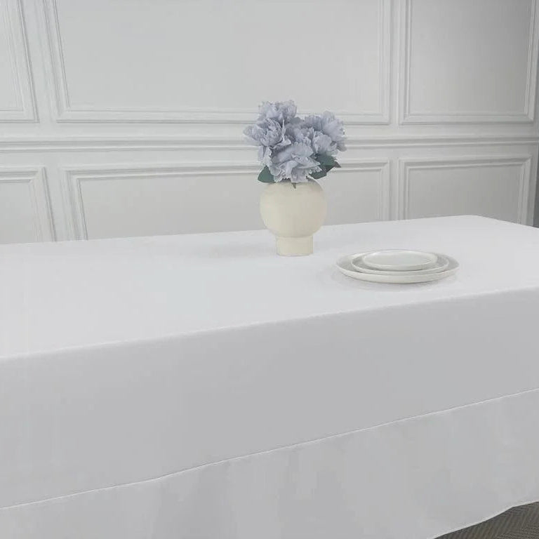 A white table with a vase of flowers, showcasing the Polycotton Tablecloth from Party Social. Perfect for any event, this lightweight tablecloth adds a cloth feel without the need for paper or plastic. Easy to wash and available in various colors and sizes, it&