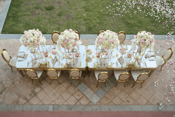 Elegant table setting with white and gold chairs adorned with fresh flowers.