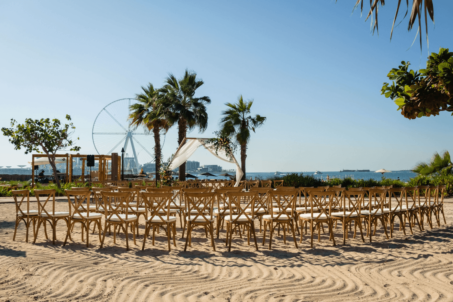 A romantic beach wedding ceremony setup on the sand with white chairs, a floral arch, and the ocean in the background.