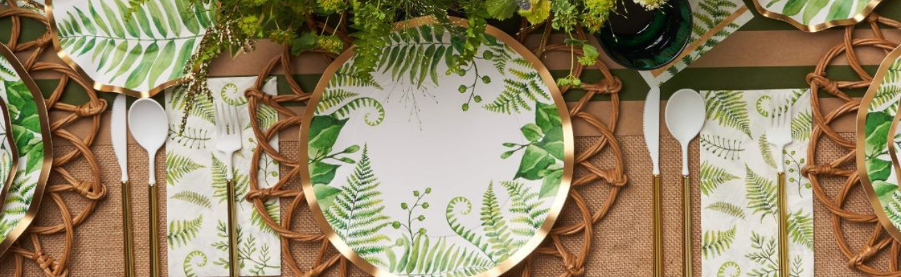 A plate with green leaves, a pen, a brush, a green glass, and a vase, showcasing party decor items.