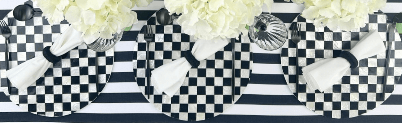Black and white checkered place setting with a white napkin and fork on a matching tablecloth, featuring a close-up of a flower in a vase.