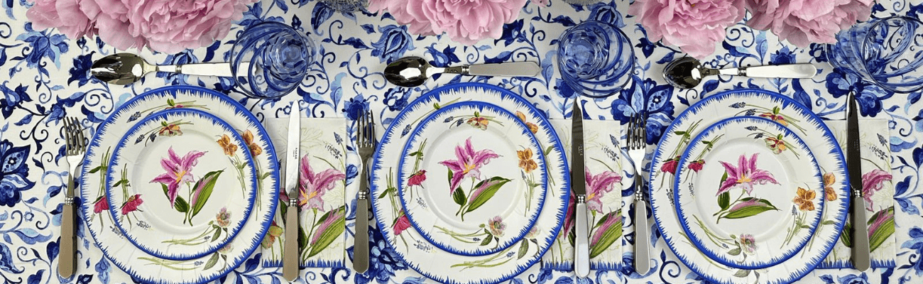 A plate with a floral design and silverware on a table, alongside a stack of similarly designed plates.