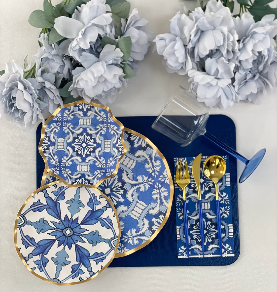 A blue and white table setting featuring patterned plates, a clear glass, and gold cutlery, suitable for elegant events and special occasions.