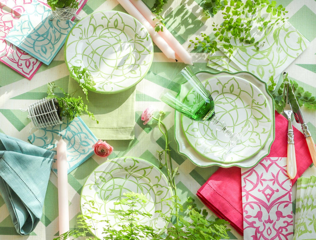 A table set with disposable paper plates, fabric napkins, glasses, and cutlery for a party.