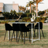 Monochromatic-Cocktail Setup: Outdoor table with eight black stools and a flower centrepiece, designed for hosting events or gatherings, available from Party Social.