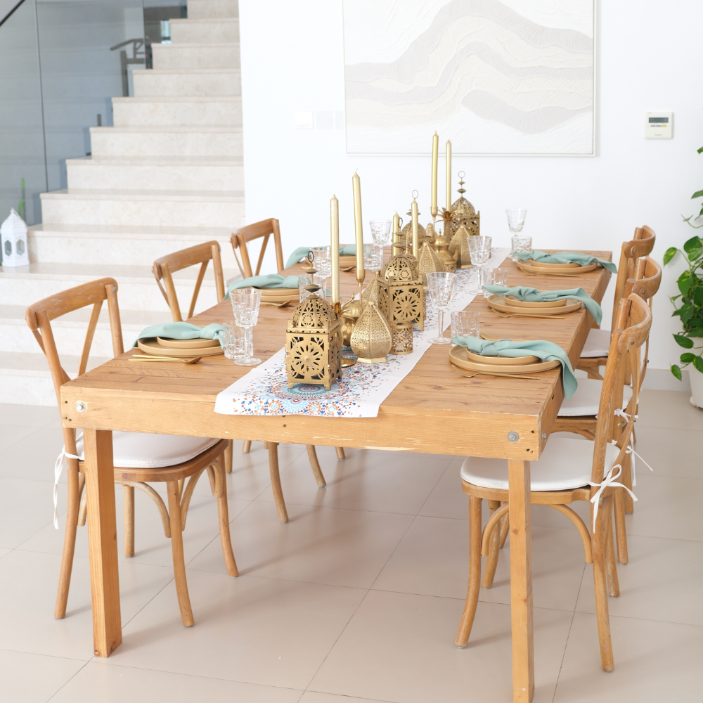 Golden Hour Iftar- Dining Setup featuring a wooden table, crossback chairs, ornate lanterns, gold cutlery, and elegant tableware for eight guests.