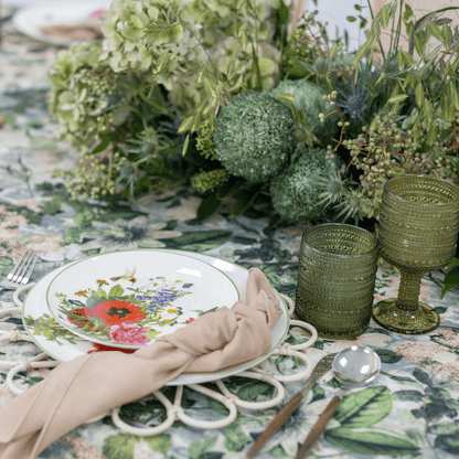 Garden Bliss - Dining Setup featuring plates, gold cutlery, rattan chargers, goblets, napkins, and a floral centerpiece on an elegantly arranged table.