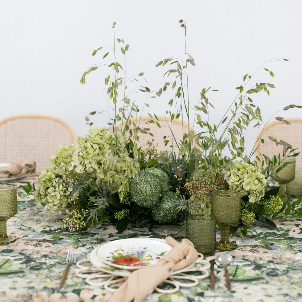 Garden Bliss- Dining Setup: Elegant table with floral centerpiece, rattan plates, gold cutlery, goblets, and rattan chairs, perfect for hosting eight guests.