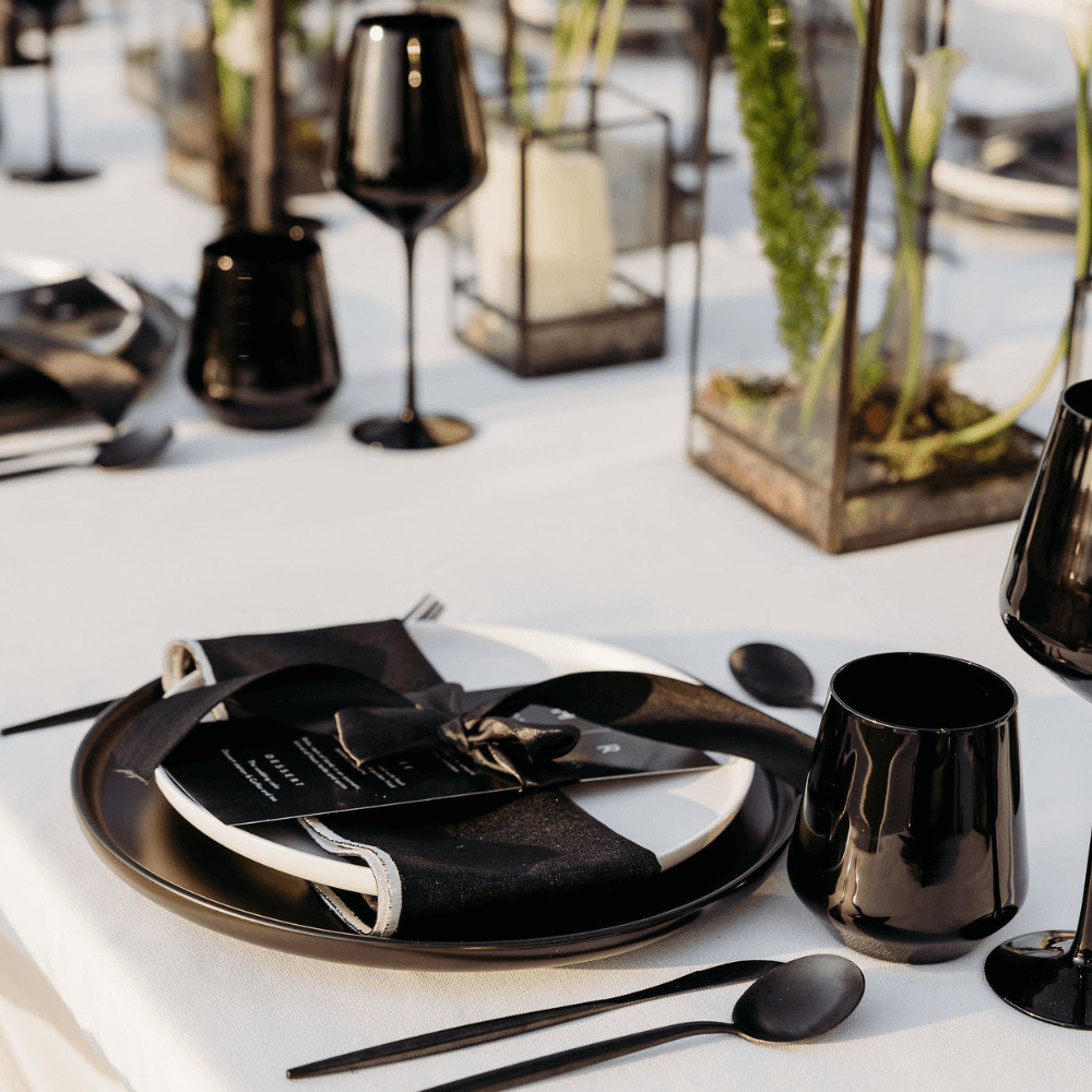 Monochromatic Dining Setup featuring black tableware, wine glasses, napkins, and vases, perfect for events. Includes plates, cutlery, and candle holders.