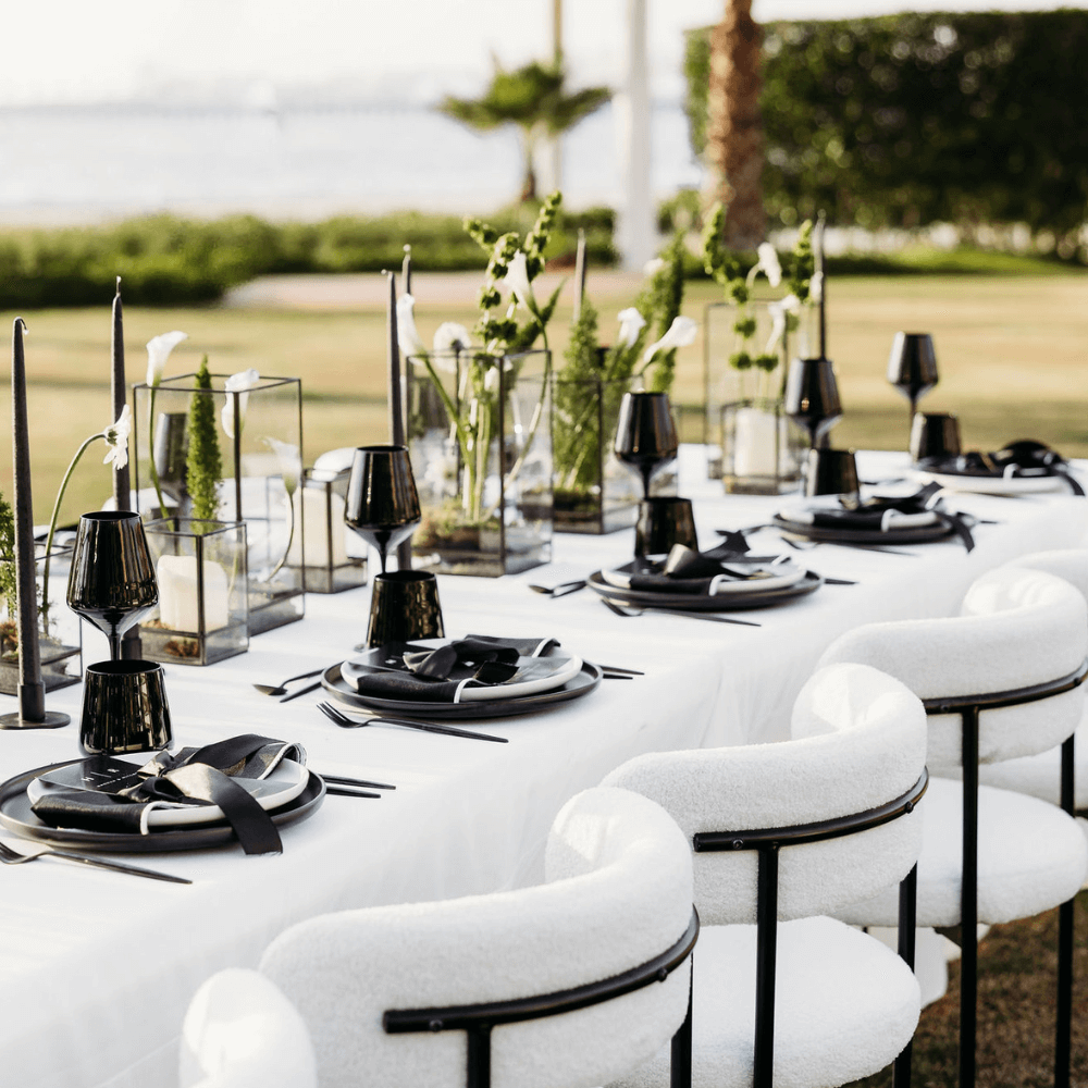 Monochromatic-Dining Setup featuring a long table with black plates, candles, wine glasses, and chairs, perfect for an elegant dinner party for eight.