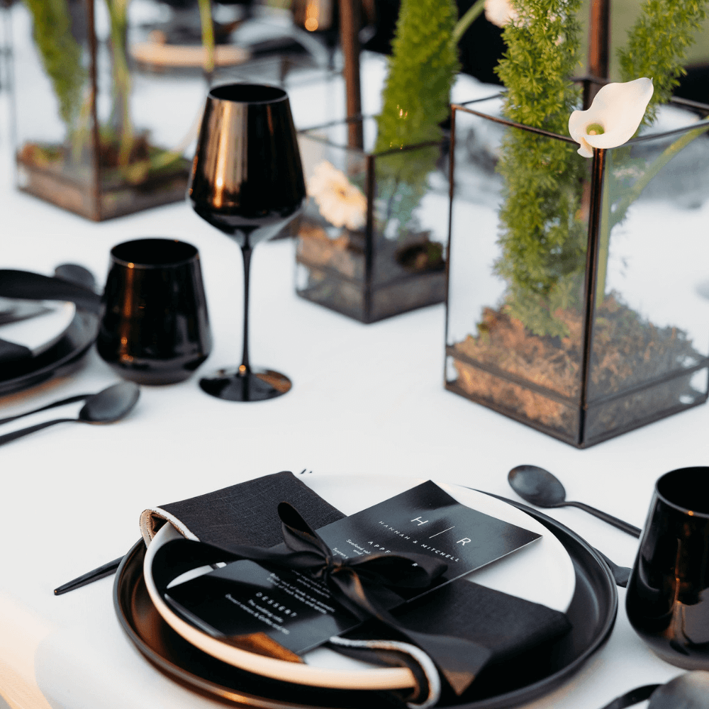 Monochromatic-Dining Setup featuring a table with black and white decorations, wine glasses, black cutlery, and flower centerpieces, ideal for an elegant dinner event.